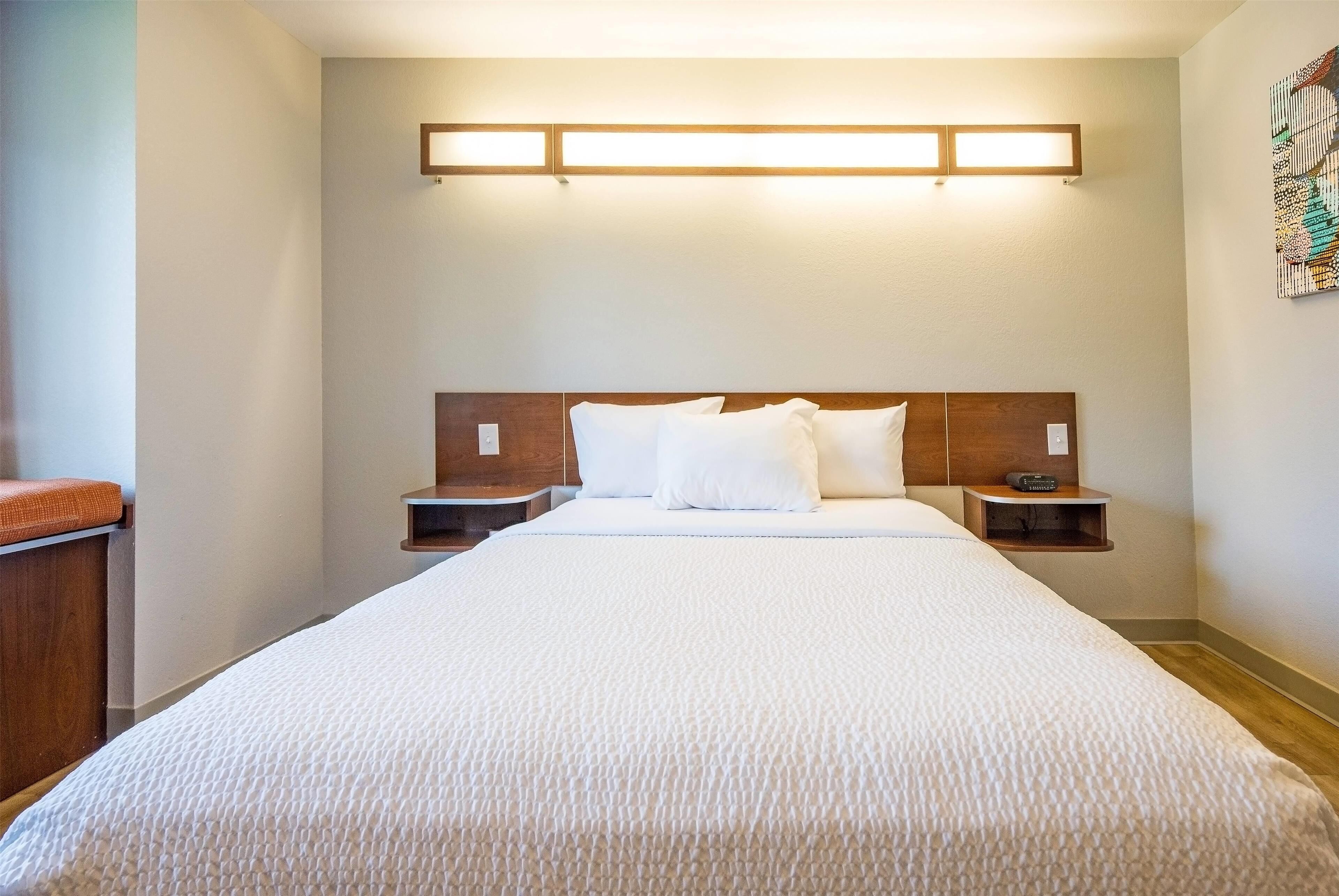 A hotel room with a large bed, wooden headboard, bedside tables, and a wall-mounted light fixture.