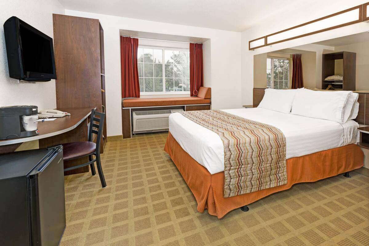 A hotel room with a bed, desk, chair, television, and a window with curtains.