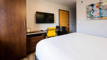A hotel room with a large bed, a desk with a chair, a flat-screen TV, a coffee maker, and a wooden wardrobe.