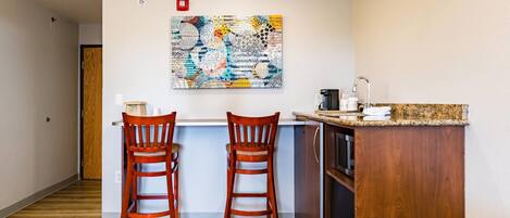 A small kitchen with two wooden chairs, a granite countertop, and a colorful abstract painting on the wall.