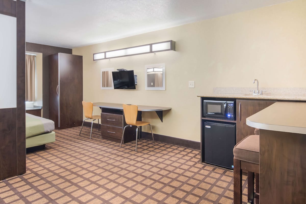 A compact hotel room with a bed, a desk, a chair, a microwave, and a sink.