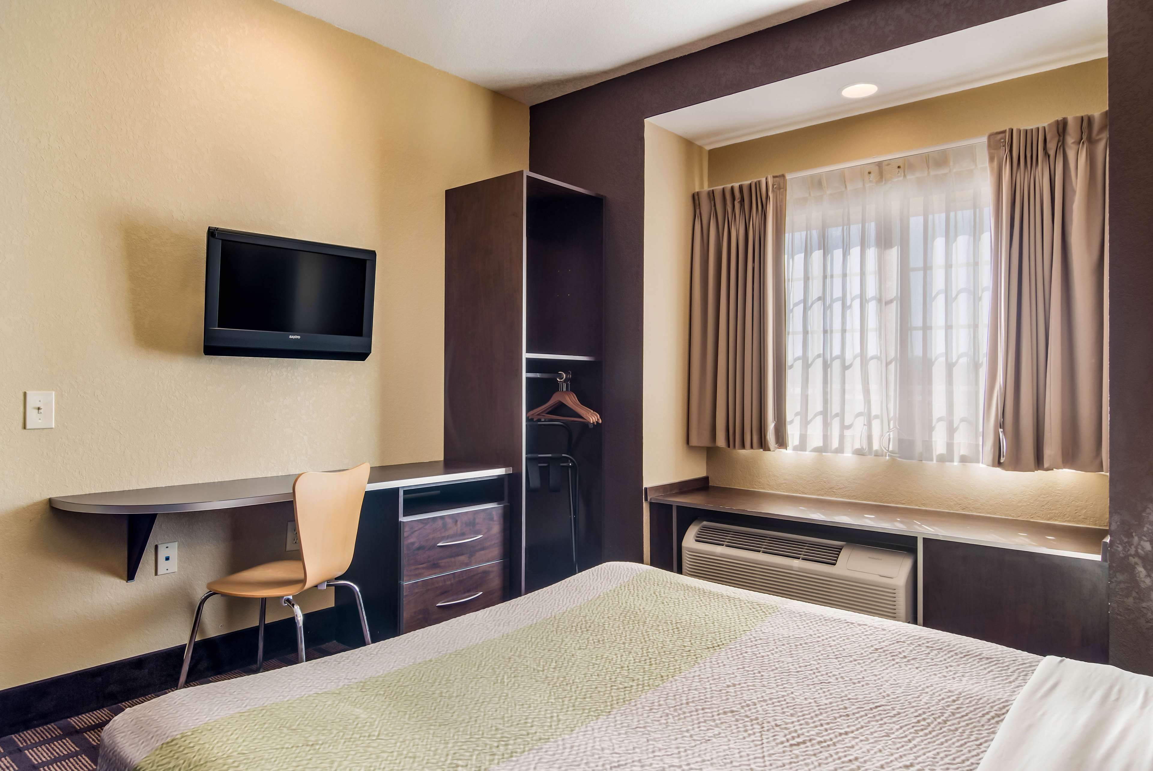 A hotel room with a bed, a desk, a chair, a TV, a wardrobe, and a window with curtains.
