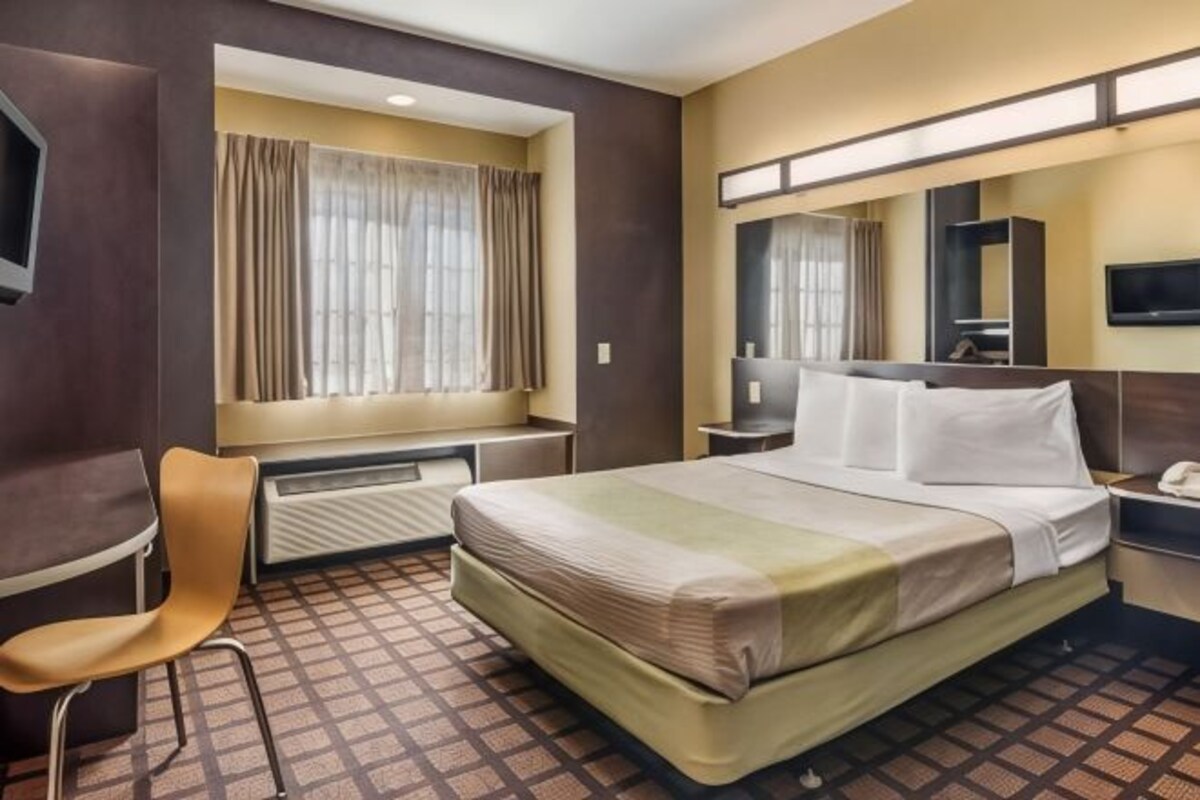 A hotel room with a bed, a desk, a chair, a TV, and a window with curtains.