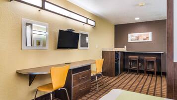 Habitación de hotel con cama, escritorio con dos sillas, televisión y una pequeña kitchenette.