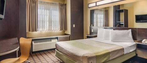 A hotel room with a bed, a chair, a desk, a television, a mirror, and a window with curtains.