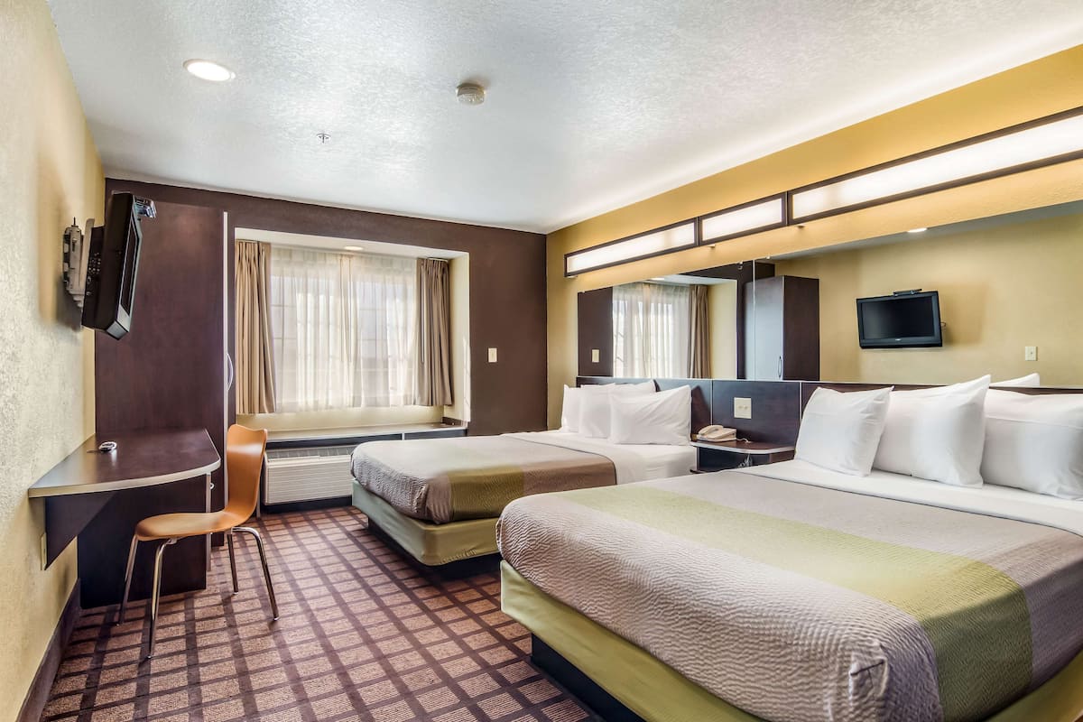A hotel room with two beds, a desk, a chair, a TV, and a window with curtains.