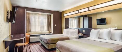 A hotel room with two beds, a desk, a chair, a TV, and a window with curtains.