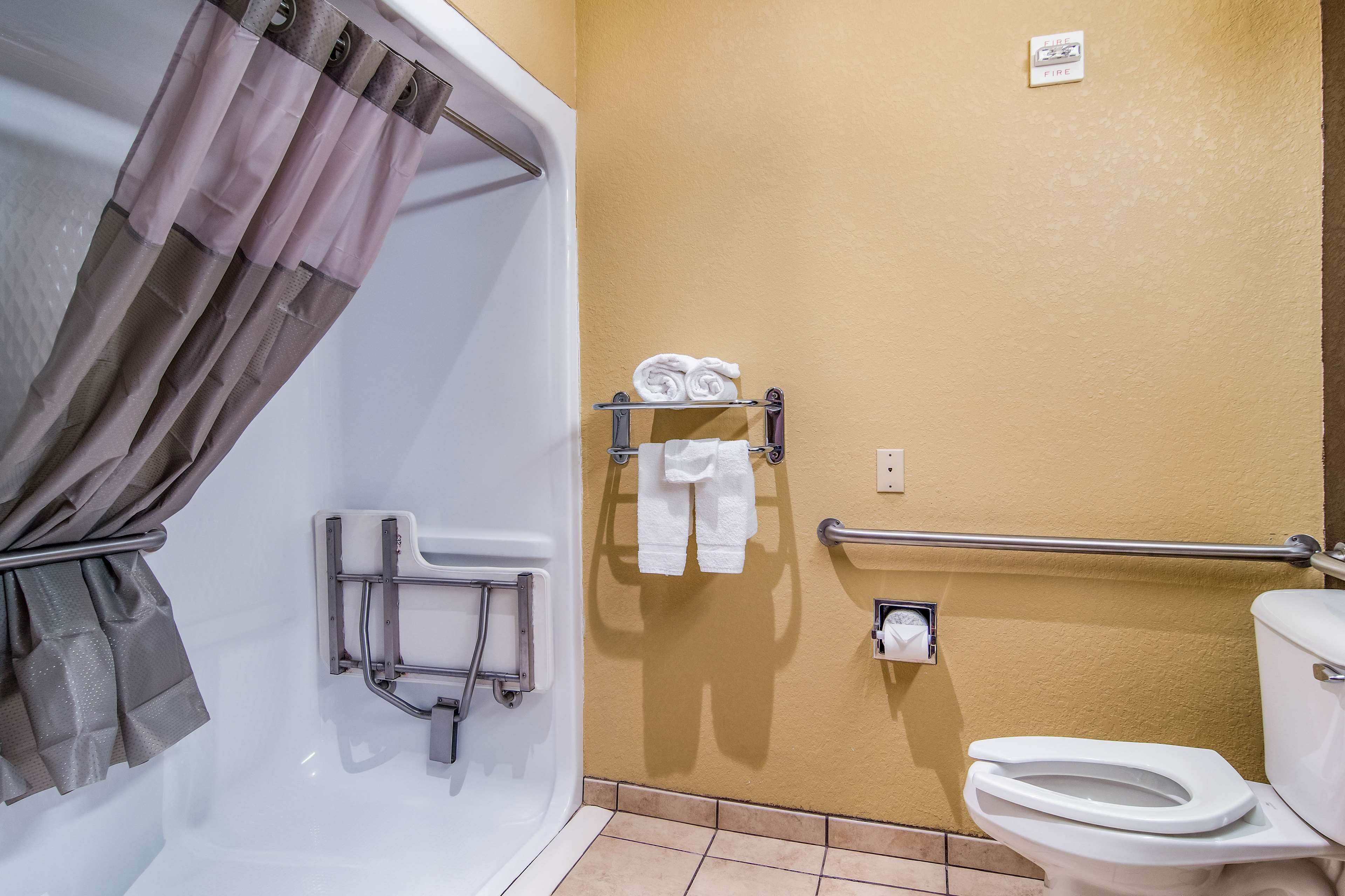 Une salle de bain équipée d’une baignoire, de toilettes, d’un porte-serviettes avec des serviettes, d’une barre d’appui et d’un détecteur d’incendie.
