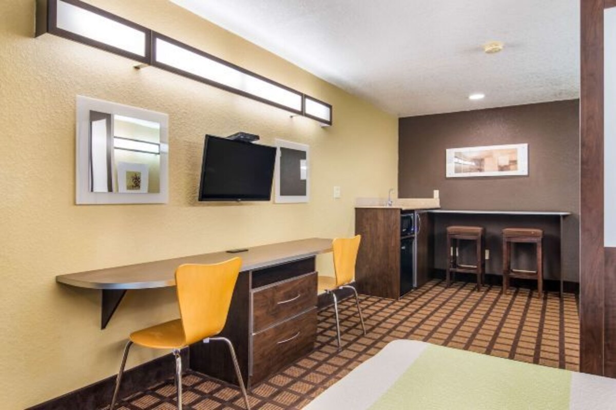 A hotel room with a bed, a desk with two chairs, a television, and a small bar area with stools.