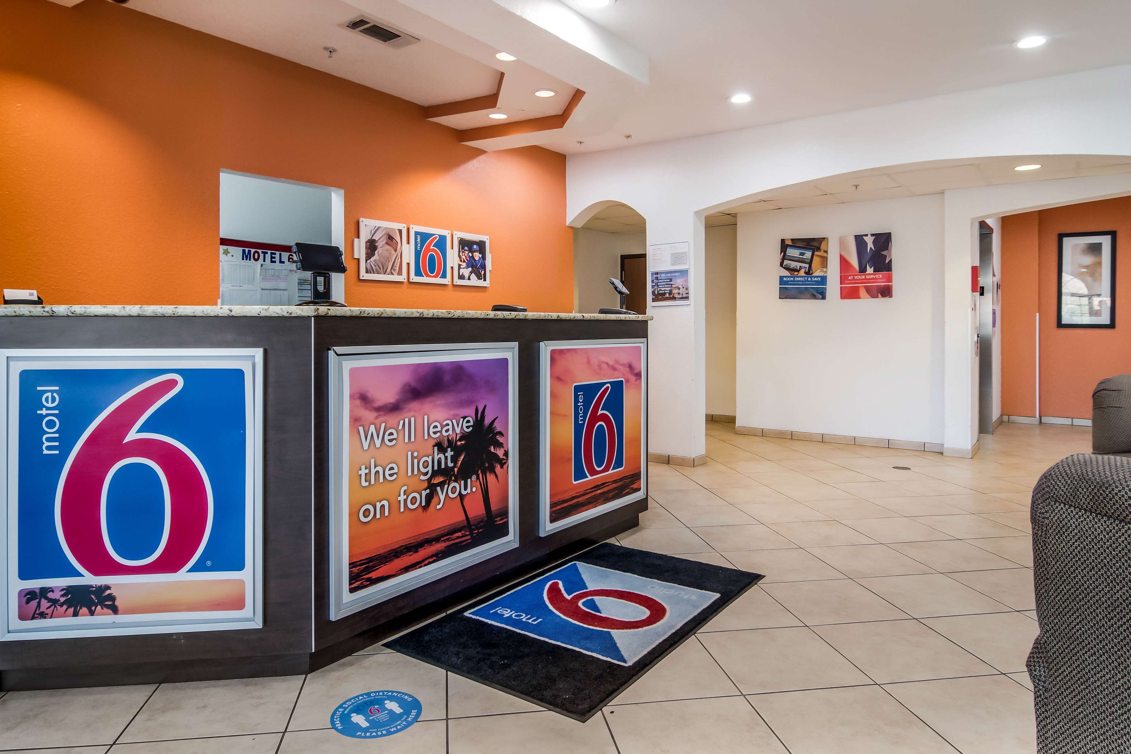 A hotel reception area with a counter, a digital screen, and a large '6' sign.