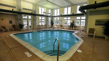An indoor swimming pool with clear water, surrounded by lounge chairs and potted plants.