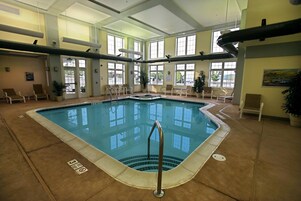 An indoor swimming pool with clear water, surrounded by lounge chairs and potted plants.