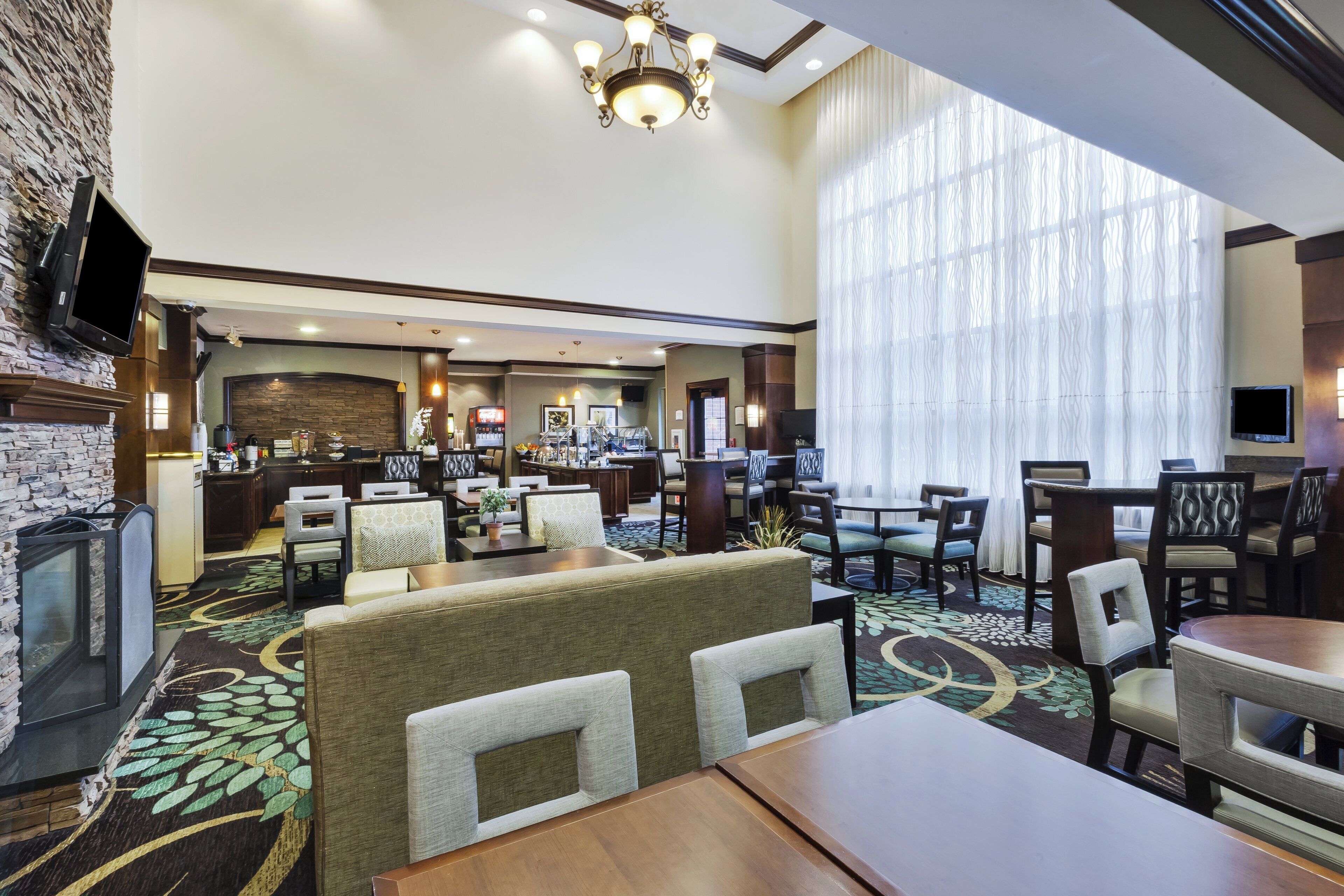 A hotel lobby with a fireplace, seating area, and a large window with curtains.