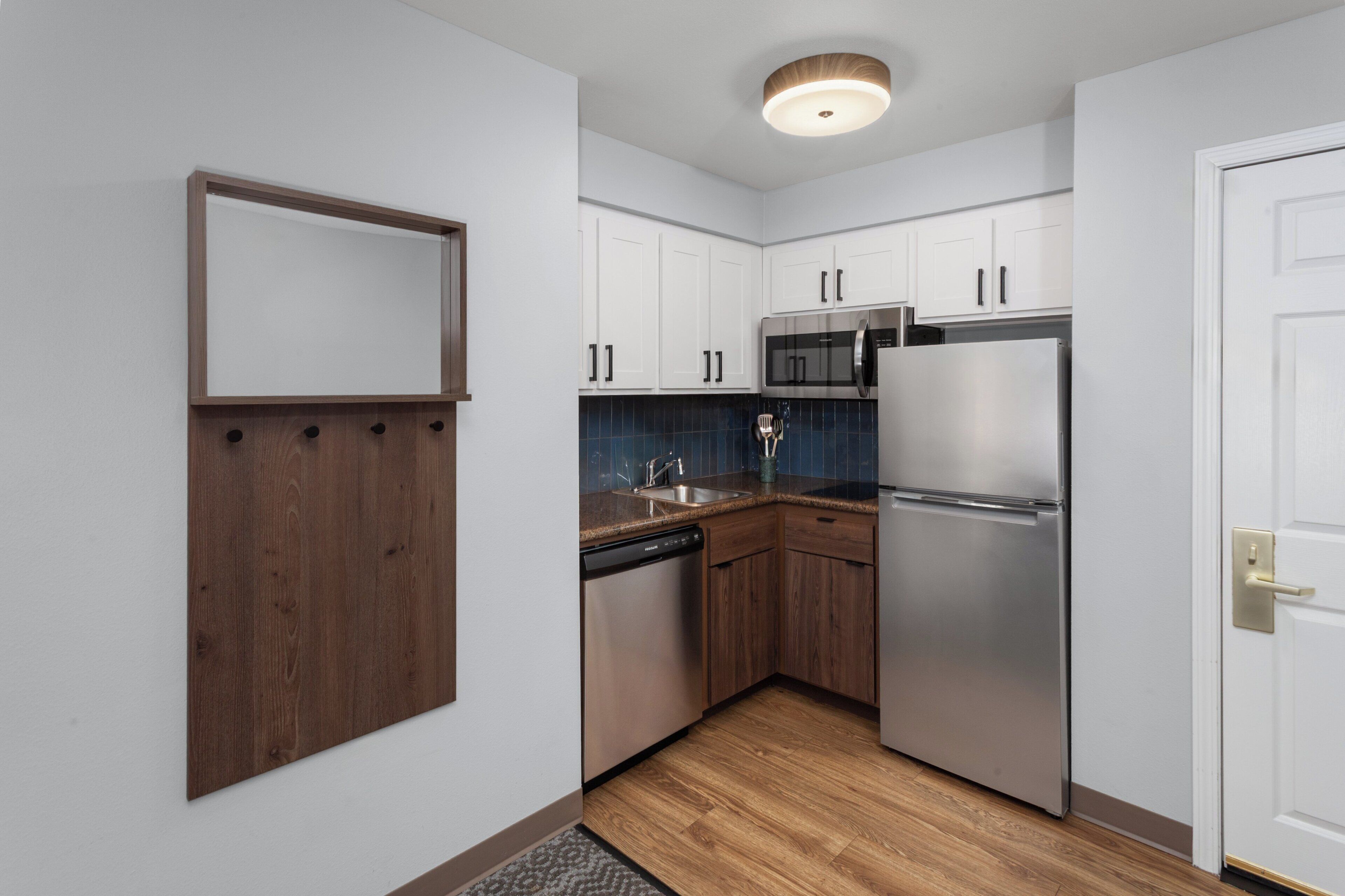A modern kitchen with white cabinets, stainless steel appliances, and a wooden floor.