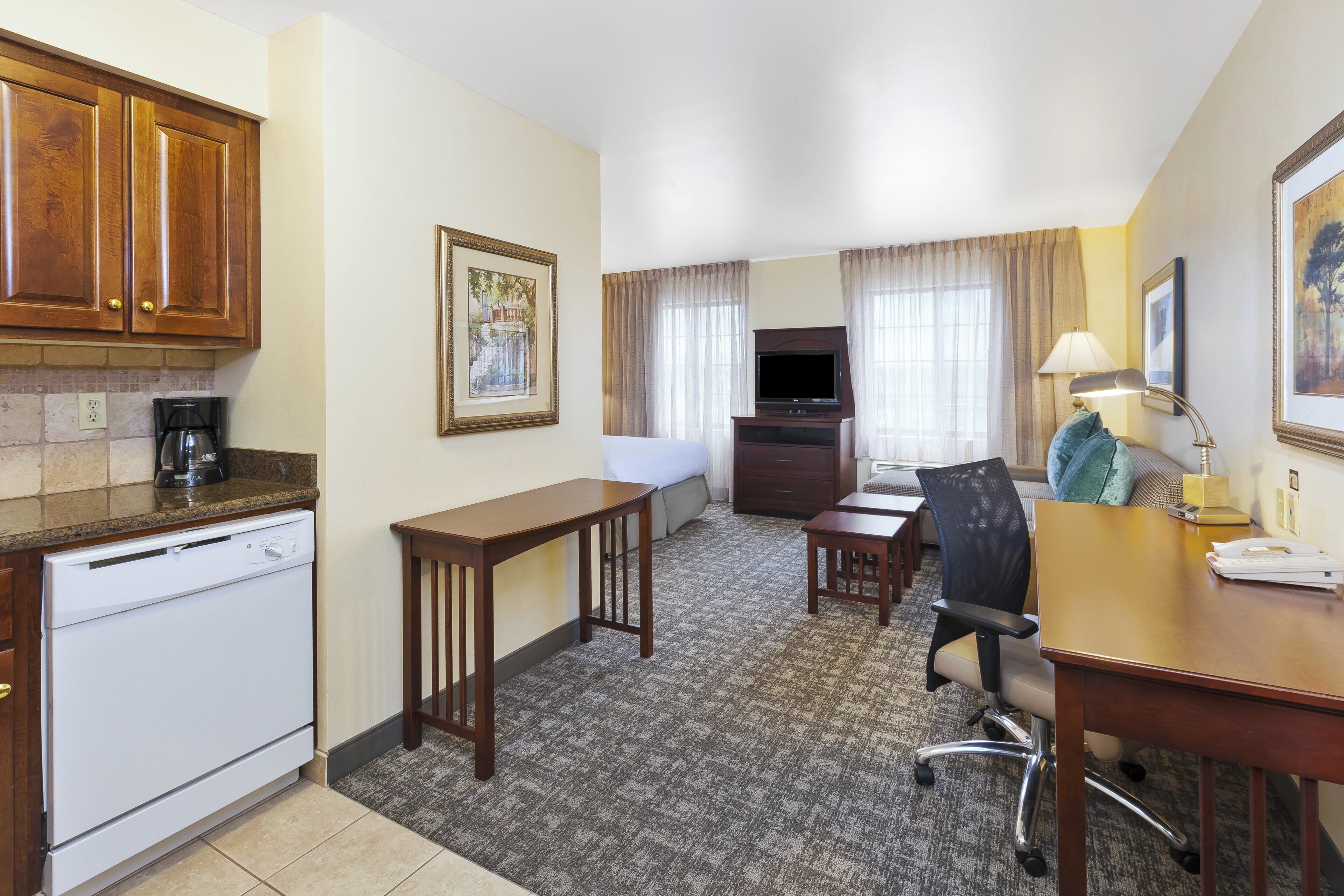 Habitación de hotel con kitchenette, una cama, un escritorio, una silla y un televisor.