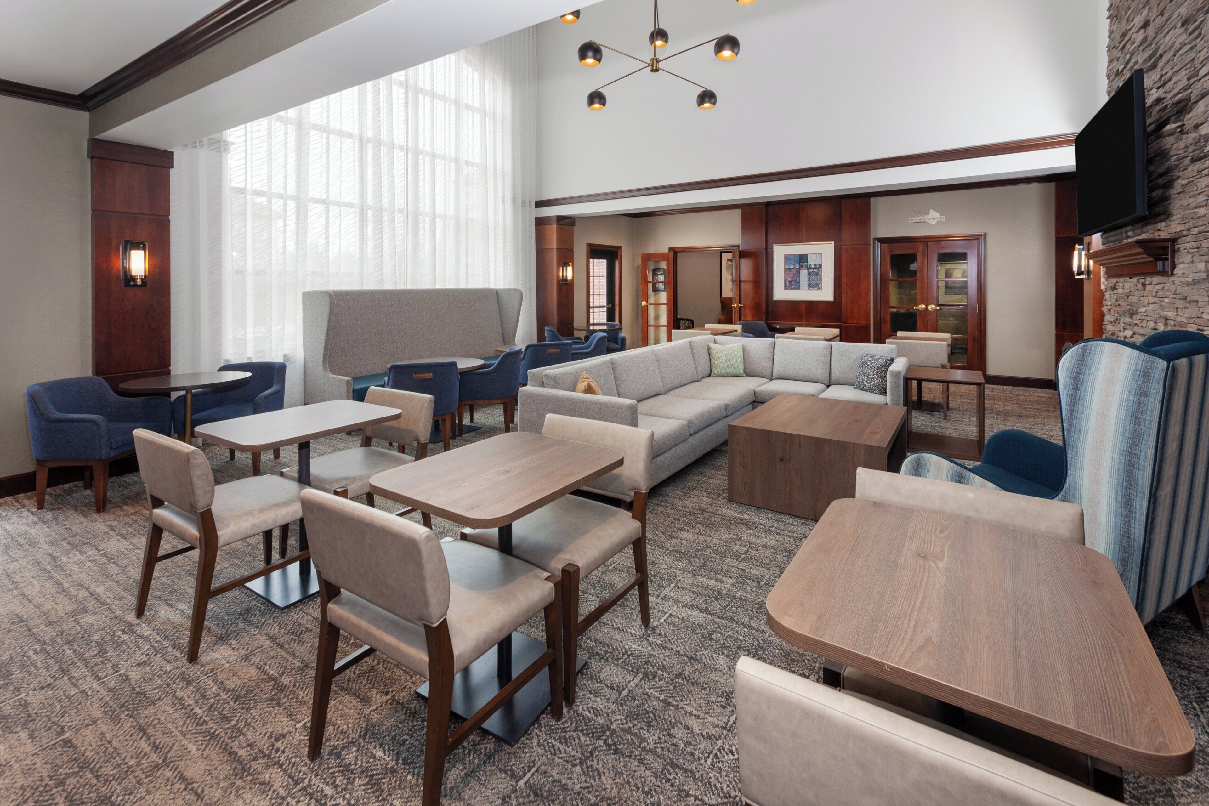Un hall d’hôtel comprenant un espace salon avec des fauteuils, des tables, un grand canapé et un téléviseur fixé au mur.