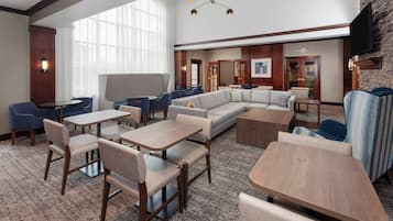Un hall d’hôtel comprenant un espace salon avec des fauteuils, des tables, un grand canapé et un téléviseur fixé au mur.