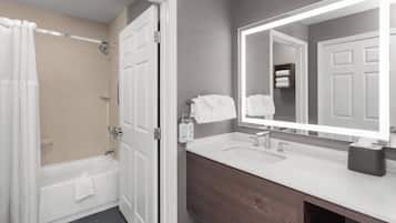 Une salle de bain moderne avec une baignoire, un grand miroir, un lavabo et un rideau de douche.