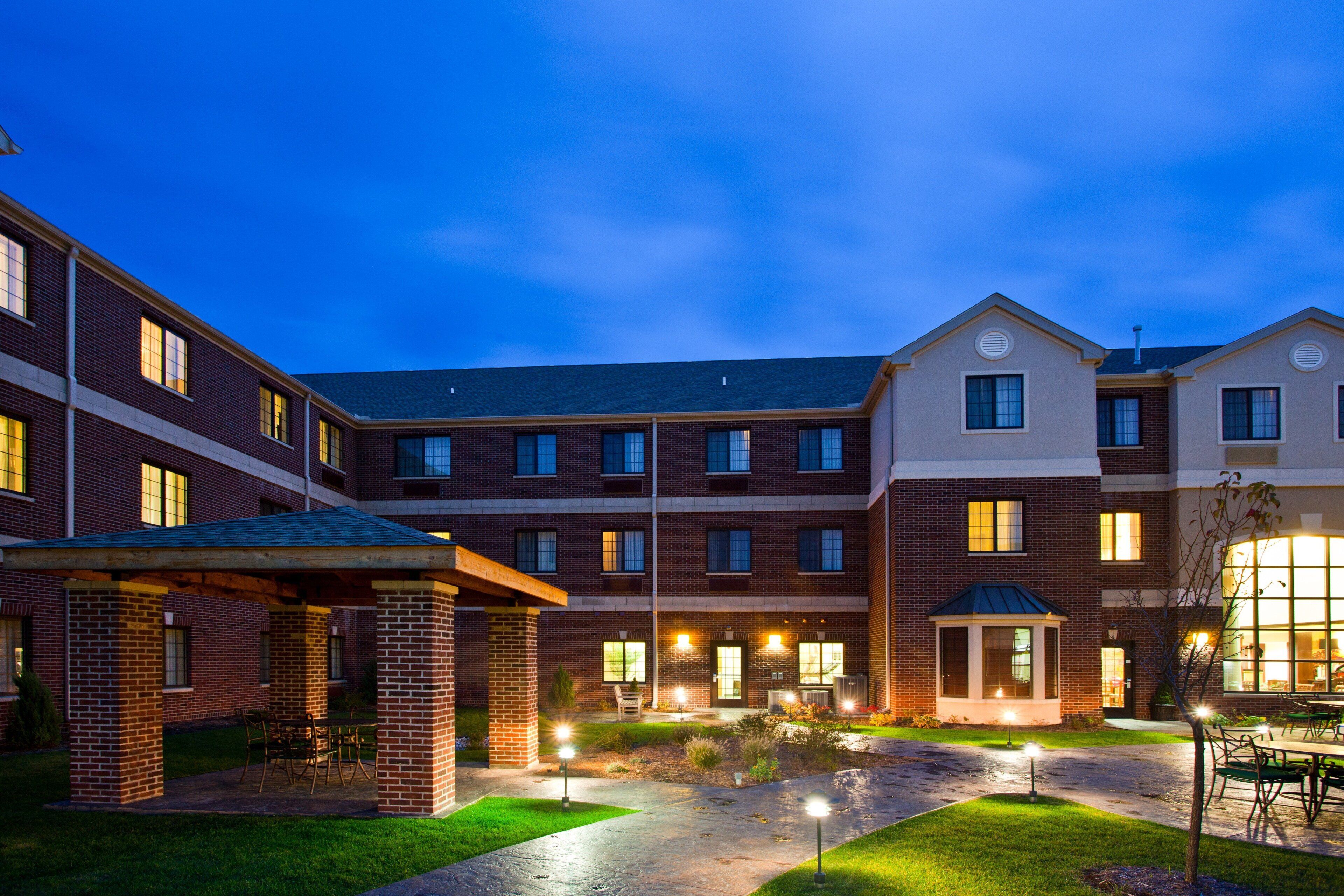 A multi-story building with a courtyard, outdoor seating, and illuminated windows.