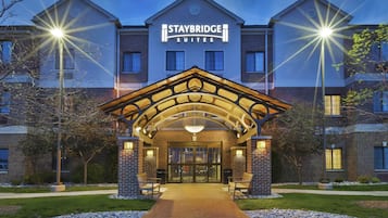 Entrada de un hotel Staybridge Suites con fachada de ladrillo, un área de acceso cubierta y un camino que lleva a las puertas principales.