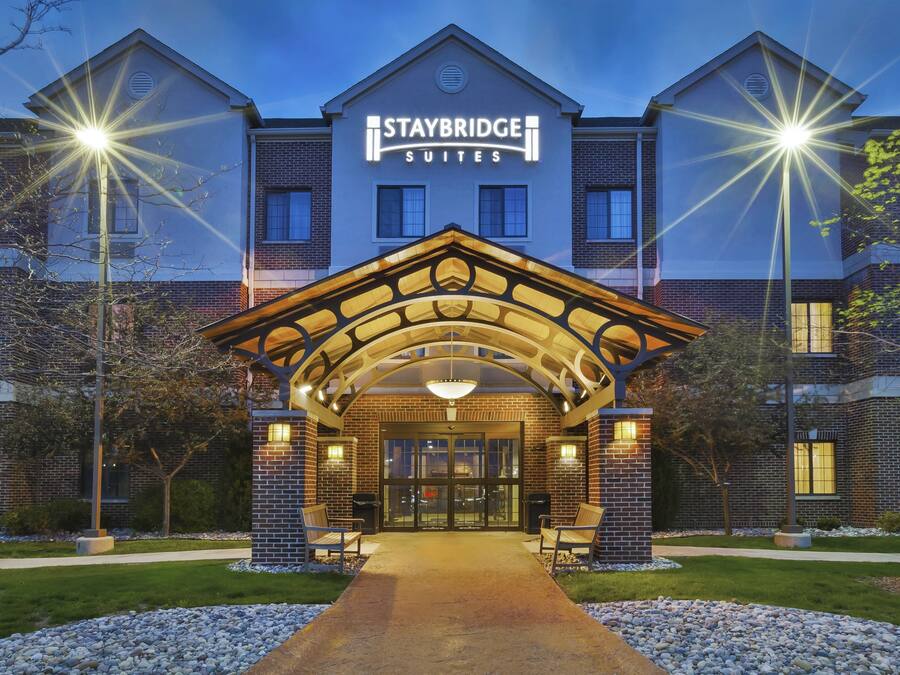 A Staybridge Suites hotel entrance with a brick facade, a covered entrance area, and a pathway leading to the main doors.