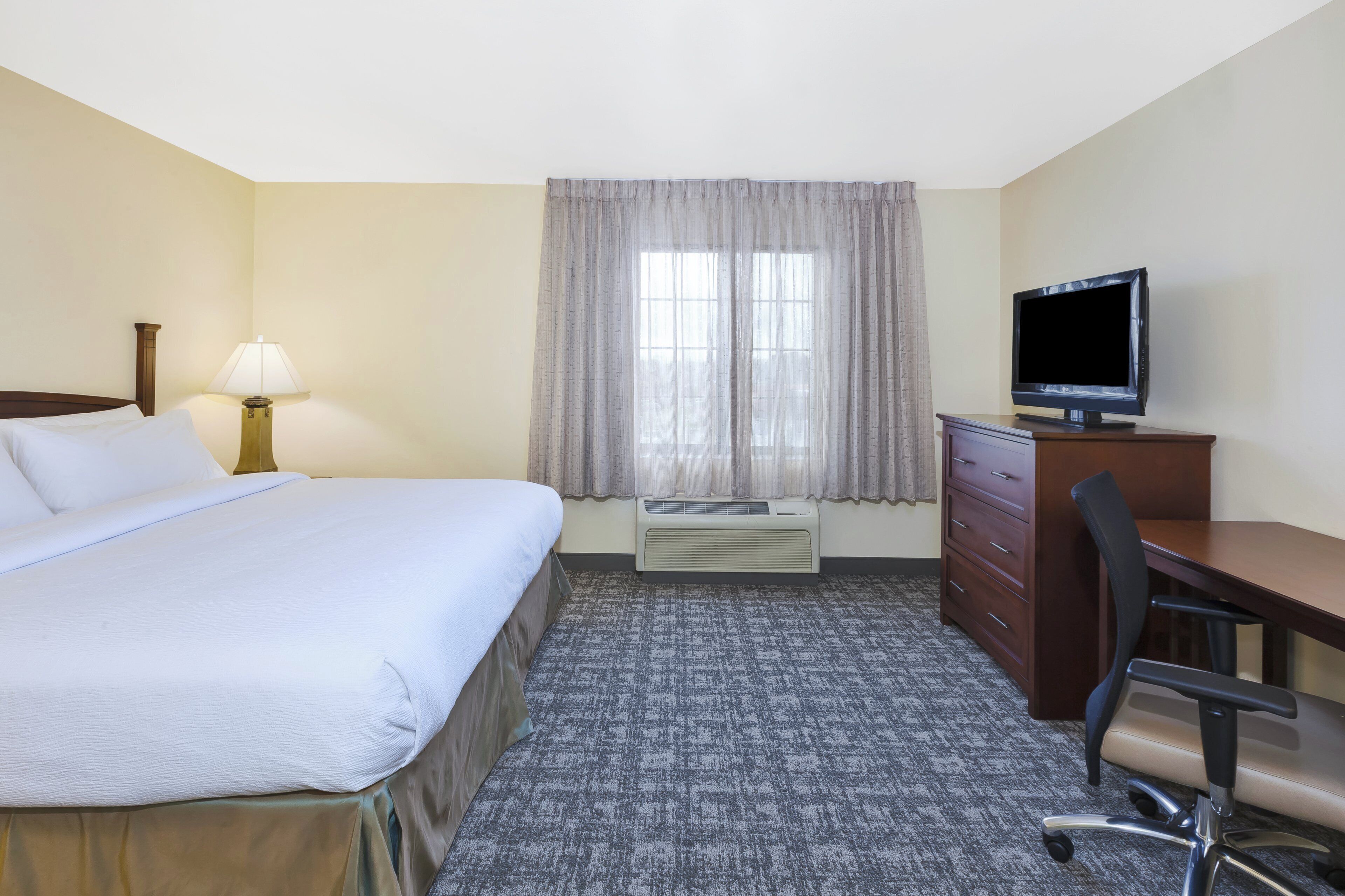 Ein Hotelzimmer mit Bett, Schreibtisch, Stuhl, Fernseher und einem Fenster mit Vorhängen.
