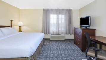 Ein Hotelzimmer mit Bett, Schreibtisch, Stuhl, Fernseher und einem Fenster mit Vorhängen.