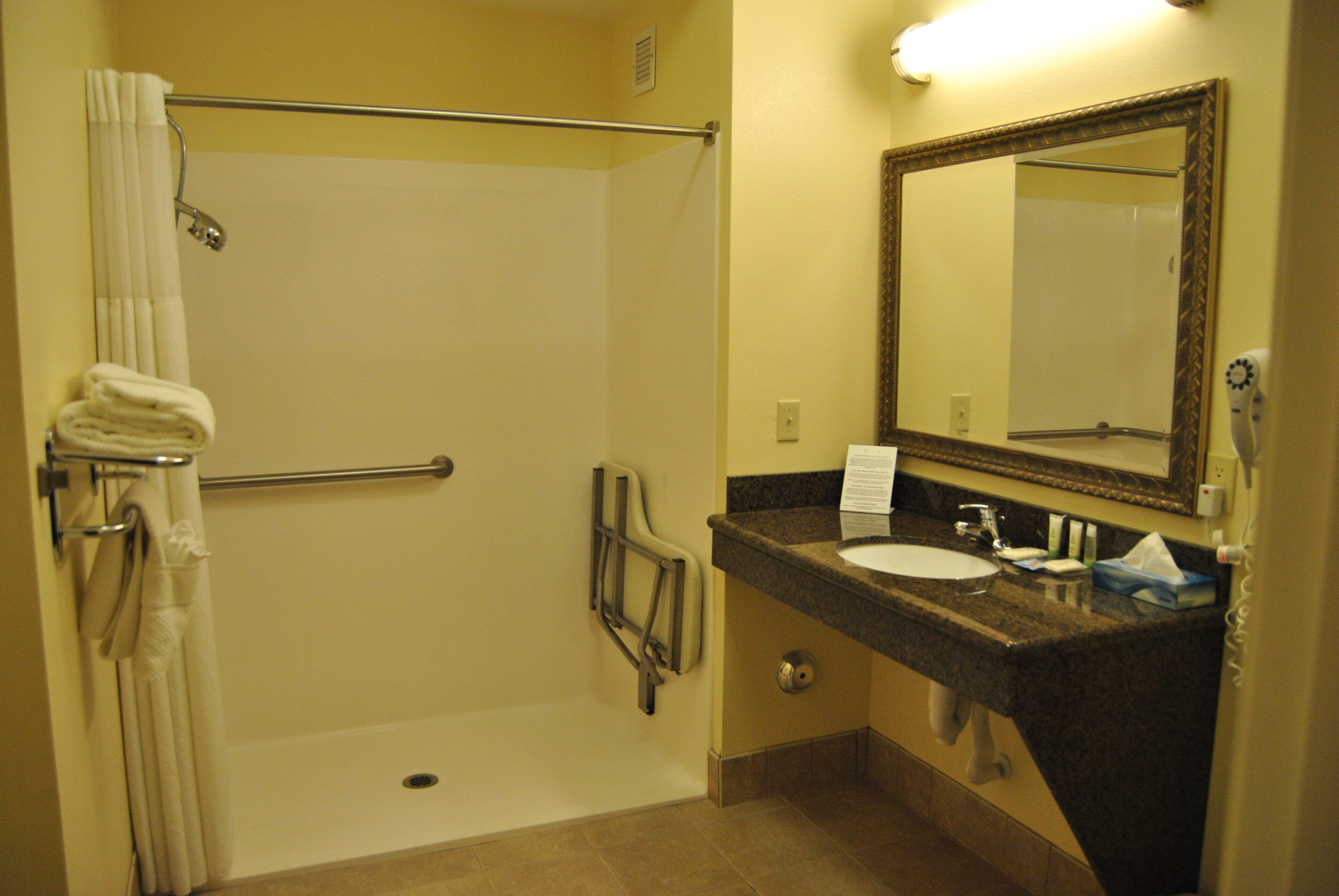 A bathroom with a shower, a sink, a mirror, and a towel rack.