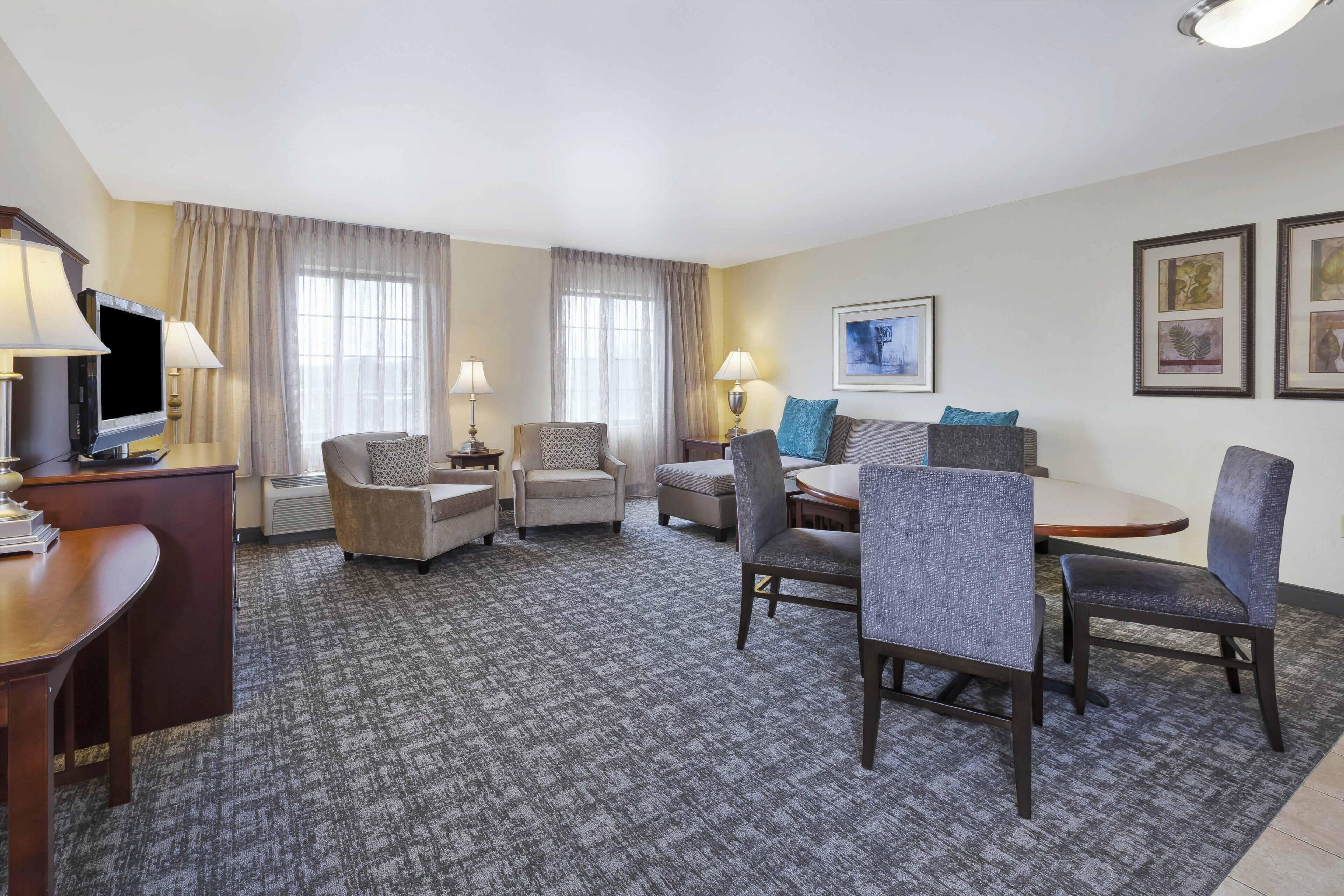 Habitación de hotel con televisión de pantalla plana, dos sillones, un sofá, una mesa de comedor con sillas y suelo alfombrado.