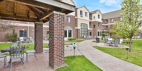 A courtyard with outdoor seating, brick pillars, and a covered area. - Staybridge Suites Lansing - Okemos by IHG (Okemos)