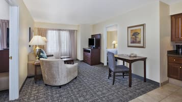 Una habitación de hotel con sofá, sillón, escritorio, televisión y un cuadro en la pared.