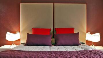 A bed with a headboard, two red pillows, two purple pillows, and a purple blanket.