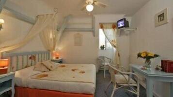 A bedroom with a bed, bedside table, TV, and a small desk with a vase of flowers.