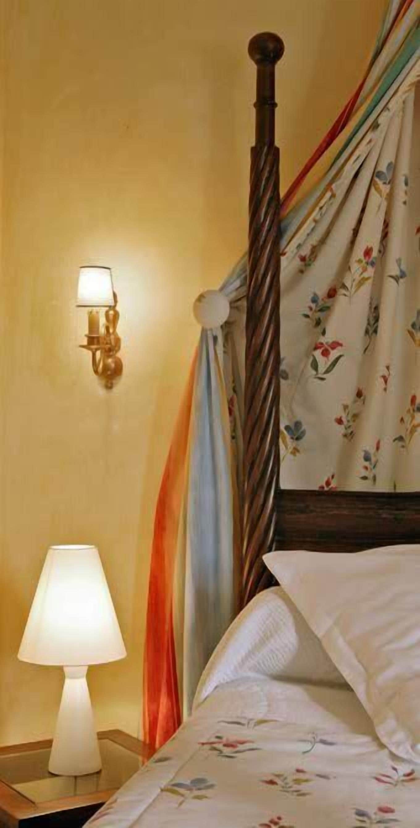 Een bed met houten hoofdbord, een nachtkastje met lamp en een wandlamp.