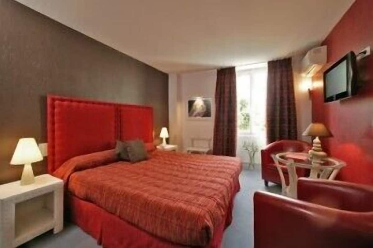 A hotel room with a large bed, a desk, a chair, and a TV.