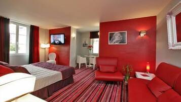 A hotel room with a bed, a red sofa, a TV, and a desk with a chair.