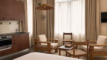 Ein Hotelzimmer mit Küchenzeile, zwei Holzstühlen, einem Bett und großen Fenstern mit Vorhängen.