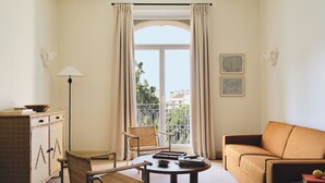 Une pièce comprenant un canapé, un fauteuil, une petite table, un meuble et une fenêtre avec des rideaux.