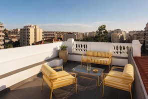 Eine Dachterrasse mit Gartenmöbeln, einem Glastisch und Blick auf die Skyline der Stadt.
