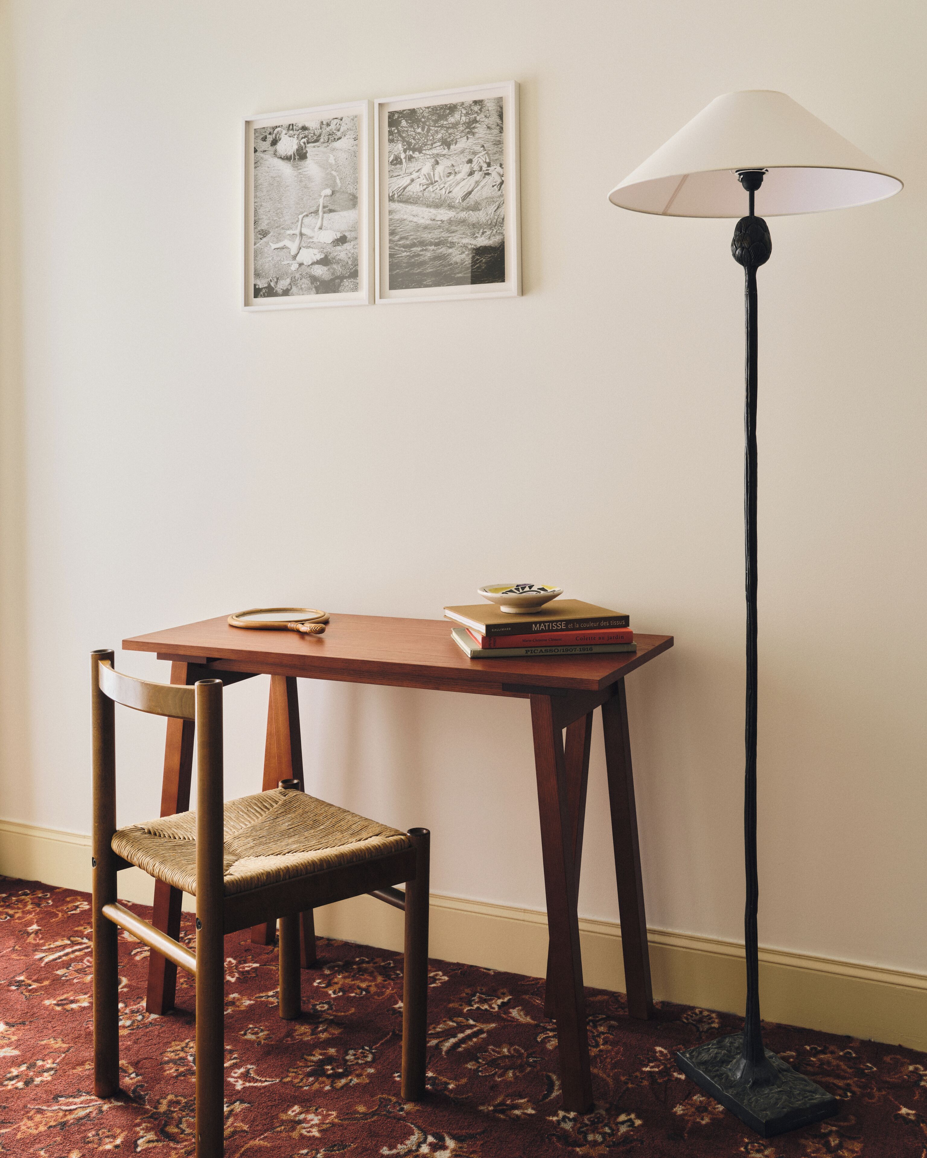 Una habitación con una mesa de madera, una silla, una lámpara de pie y dos cuadros en la pared.