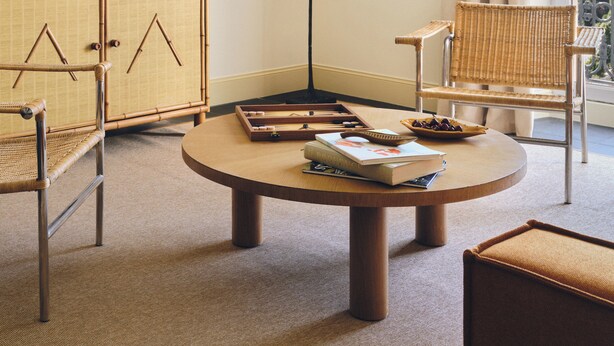 Une pièce avec une table ronde en bois, deux chaises en osier, un lampadaire, un meuble et une vue par la fenêtre.