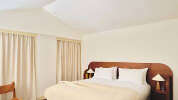 A hotel room with a bed, a chair, a nightstand with a lamp, and a window with curtains.