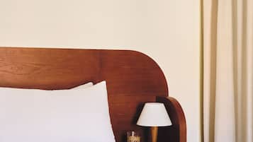 Een bed met witte beddengoed, een houten hoofdbord, een bedlampje en een wandlamp.