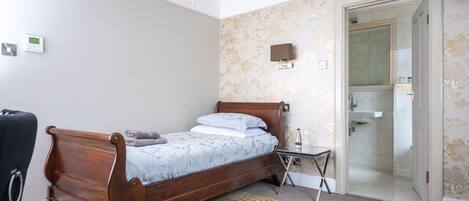 A bedroom with a wooden bed, a small bedside table, a chair, and a bathroom visible through an open door.