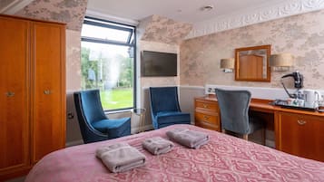 Habitación de hotel con una cama grande, dos sillones, un escritorio, un armario y un televisor en la pared.