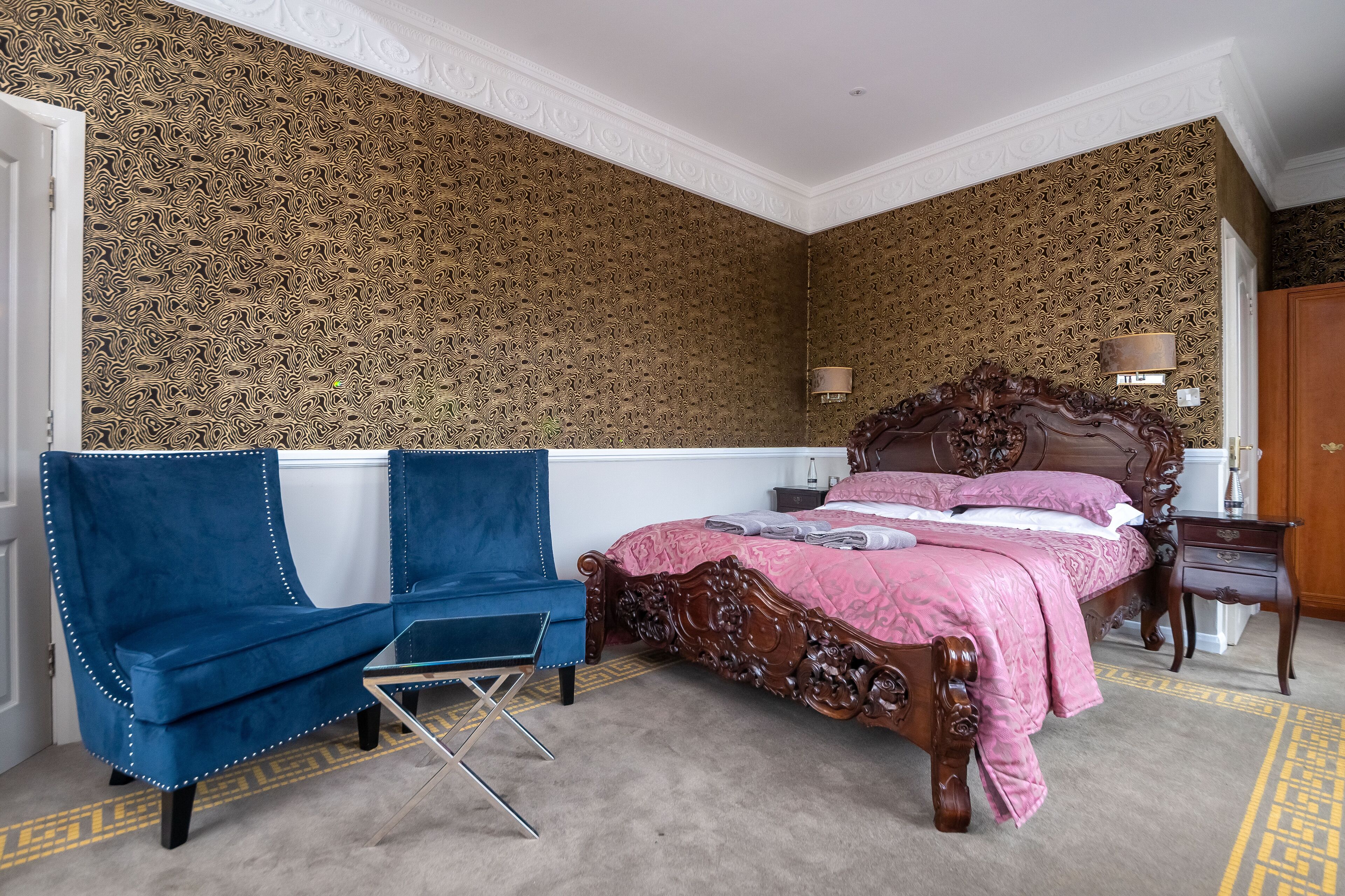 A bedroom with a large bed, a blue armchair, a small table, and a lamp.