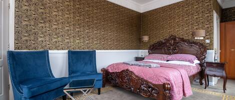 A bedroom with a large bed, a blue armchair, a small table, and a lamp.