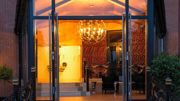 Une entrée moderne avec une façade en verre, un grand lustre et un escalier menant à l’intérieur du bâtiment.