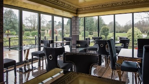 Un espace intérieur vaste et lumineux, doté de grandes fenêtres, de chaises à l’assise rembourrée de tissu noir et d’une table en verre.