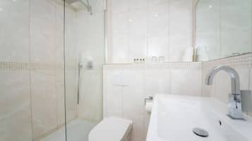 Ein modernes Badezimmer mit einer gläsernen Duschkabine, einer weißen Toilette und einem großzügigen Waschbecken mit Spiegel.